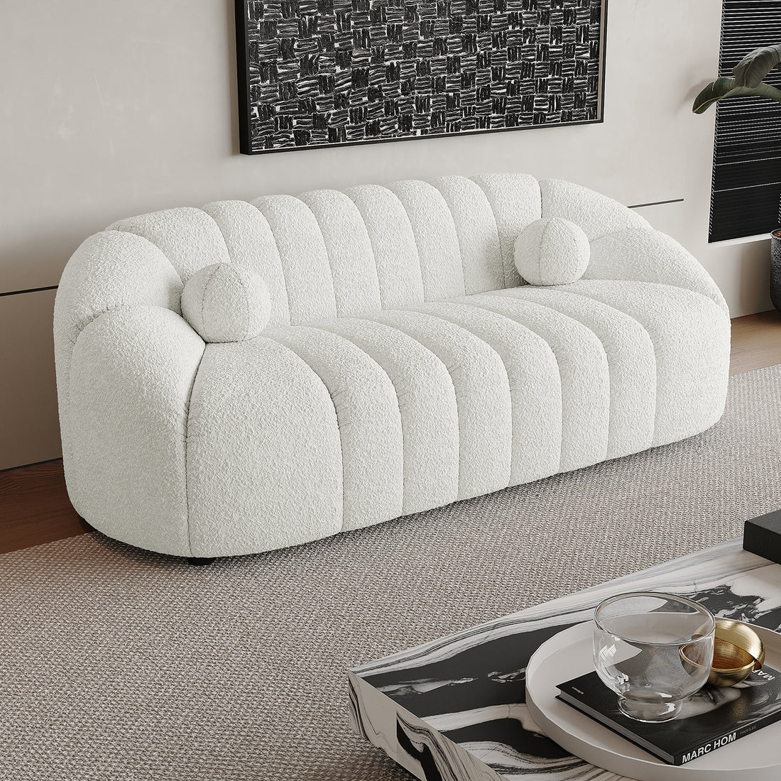 Trina 3 Seater Boucle Sofa with Pillows in Cream White, featuring channel-stitched upholstery, two round bolster pillows, on a neutral rug, with a marble coffee table and abstract painting behind.
