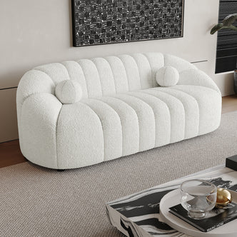 Trina 3 Seater Boucle Sofa with Pillows in Cream White, featuring channel-stitched upholstery, two round bolster pillows, on a neutral rug, with a marble coffee table and abstract painting behind.