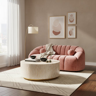 Trina 2 Seater Tufted Curved Velvet Sofa in Blush features plush channel-tufted upholstery, curved design, and bolster pillows, set in a styled living room with a round coffee table and floor lamp.