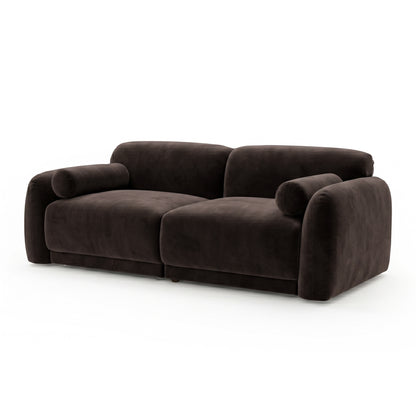 Dark brown velvet sofa with rounded armrests and cylindrical bolster pillows on white background
