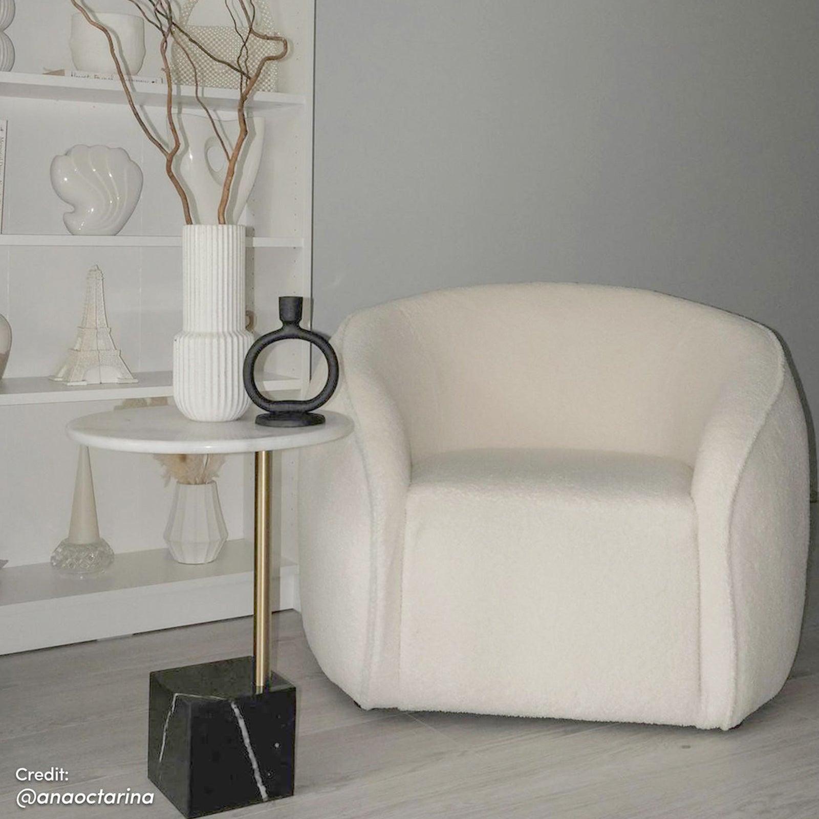 Yara Bouclé Accent Chair in Cream White, featuring a low, rounded design with textured upholstery, next to a marble-topped side table with decorative ceramic vase and branches, set in a minimalist living space.