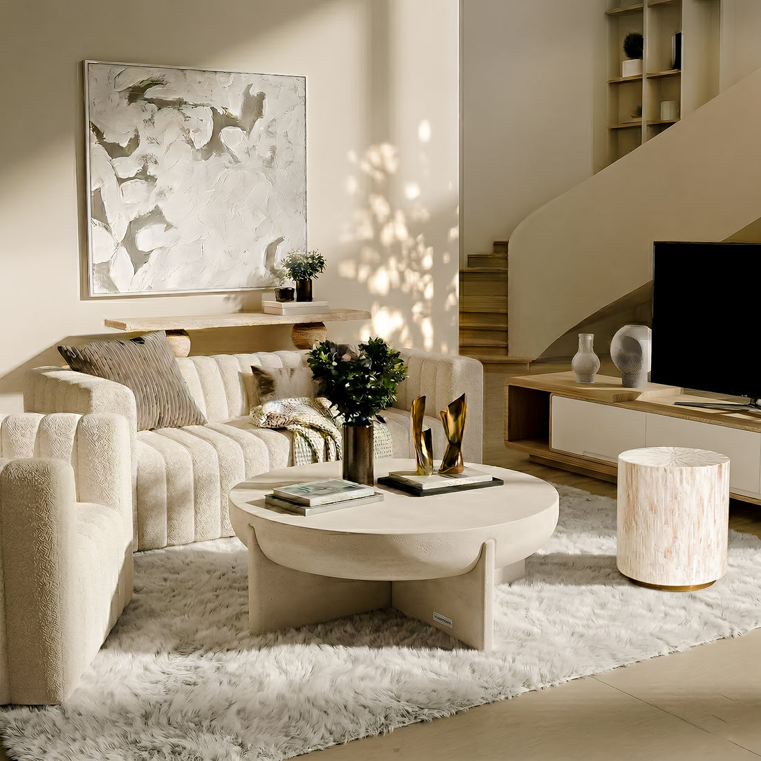 Japandi-style living room with a cream fluted sofa and armchair, a heavy circular concrete coffee table, and a luxurious white shag rug. Features an abstract canvas wall art, a floating wood console shelf, and a white minimalist TV stand near a sculptural staircase.