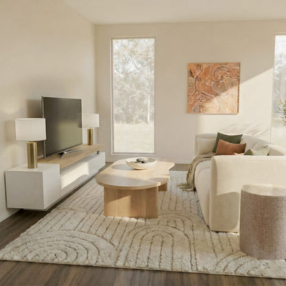 Organic modern living room featuring a cream-colored sofa with earth-tone pillows, a light oak kidney-shaped coffee table, and a textured cream area rug. A large wall-mounted flat-screen TV sits on a white and oak minimalist entertainment unit flanked by modern globe lamps.