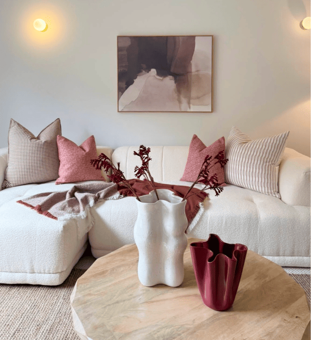 White sectional sofa with pink cushions and round timber coffee table