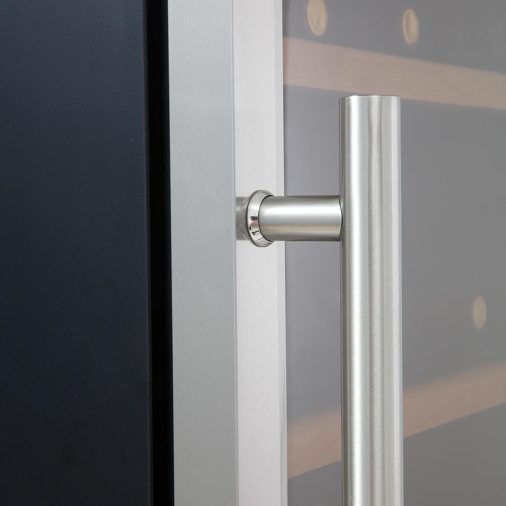 Close-up of G180D 180 Bottle Dual Zone Wine Fridge's stainless-steel tubular pull handle on a glass door. Visible behind are wooden slatted shelves holding wine bottles, suggesting refrigeration.