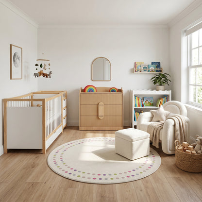 A nursery featuring a white and natural wood crib, a fluted-wood dresser, a cream bouclé chair with ottoman, and a round rug with colorful polka dots.