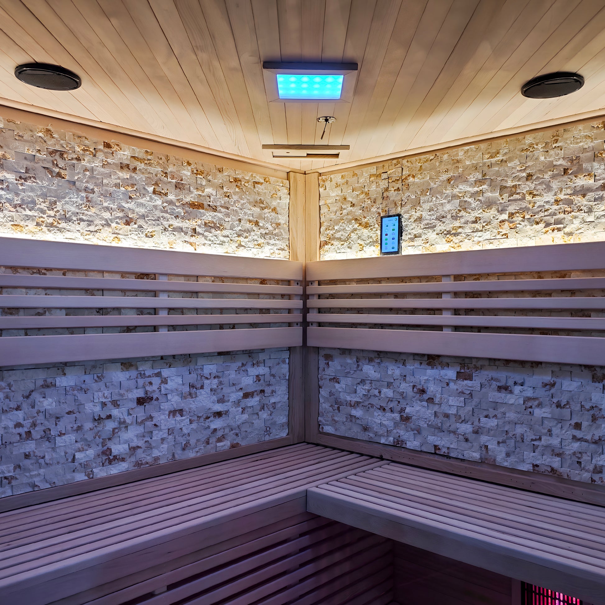 Corner of a modern sauna interior with wood benches, stone walls, and blue LED lighting.