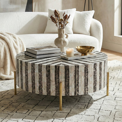 Round black and white striped coffee table styled in a living room with sofa, books, vase and decorative objects