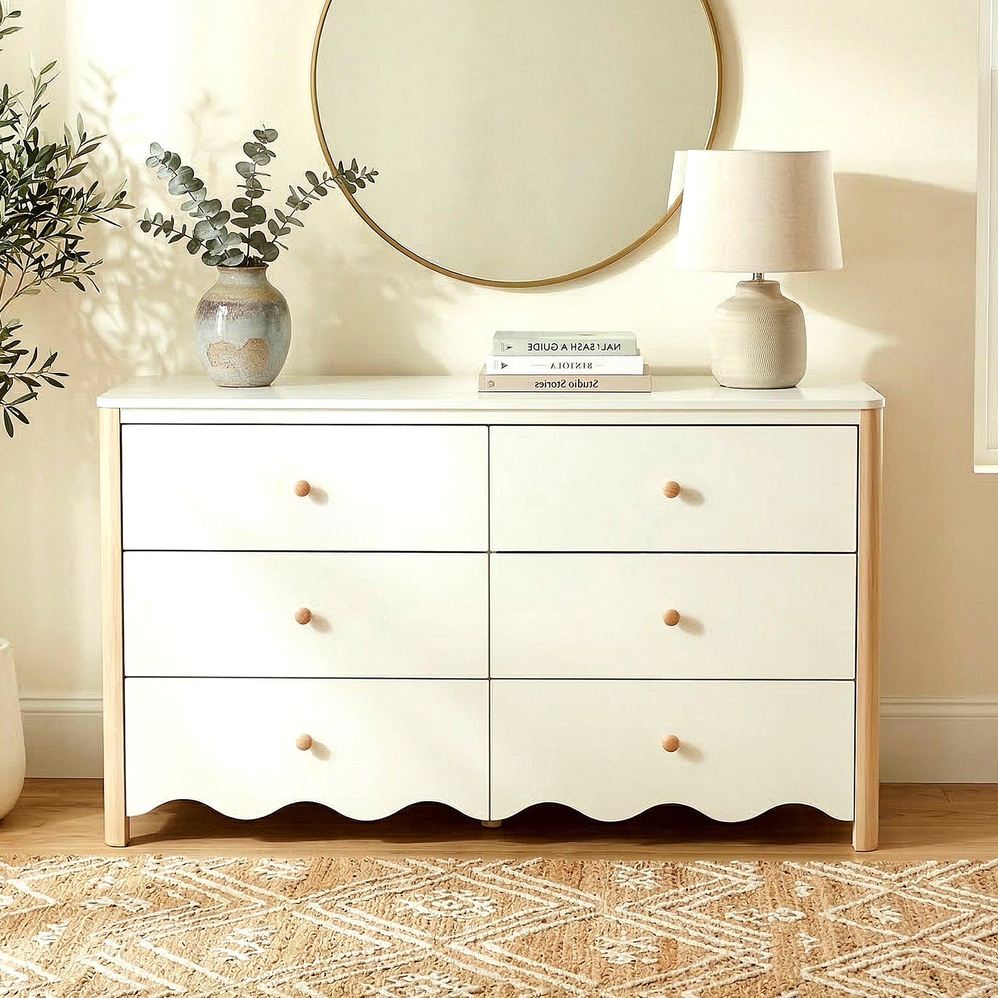 White and wood six-drawer dresser staged with books, vase, and lamp in a modern room
