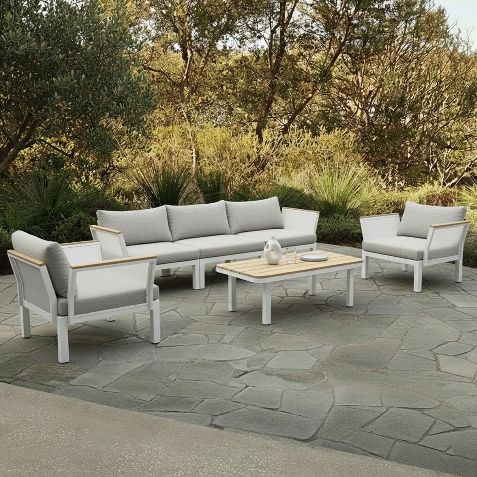 Sierra Outdoor Lounge Set in Grey on a stone patio, featuring a three-seat sofa, two armchairs with white frames, gray cushions, wood accents, and a slatted coffee table.