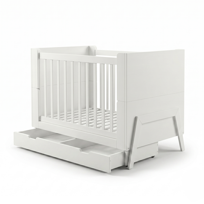 White crib on white background angled showing slats and pull-out drawer