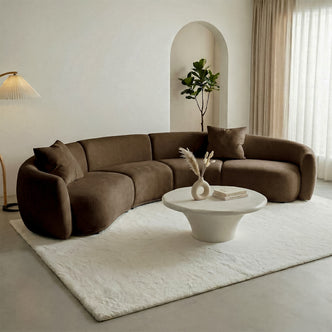 Curved sectional sofa in a styled living room with rug, coffee table, and decor