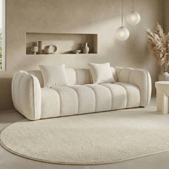 Cream-colored textured sofa with throw pillows in a modern living room setting with pendant lights and a decorative rug