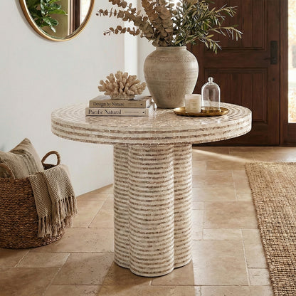 Round stone entryway table styled with decorative vases, books, and candle in a home interior