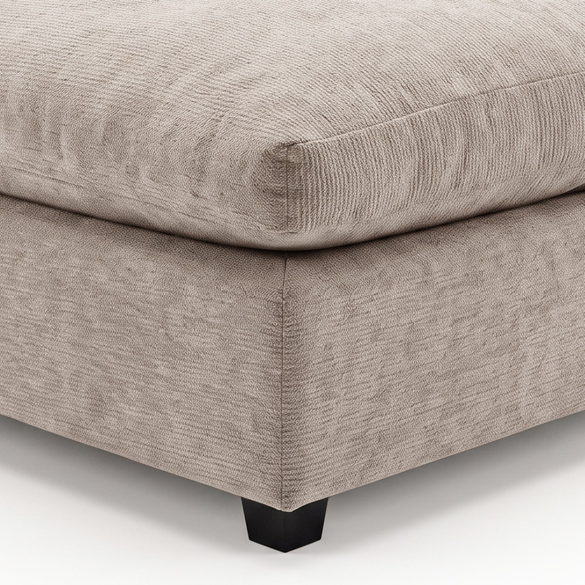 Close-up of a beige upholstered ottoman corner on a white background.