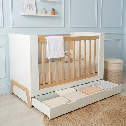 Baby crib in a decorated nursery room with storage drawer and toys