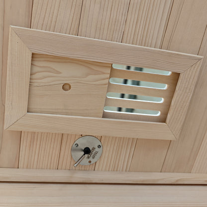 Wooden vent cover with a round metal control dial on a wood-paneled surface.