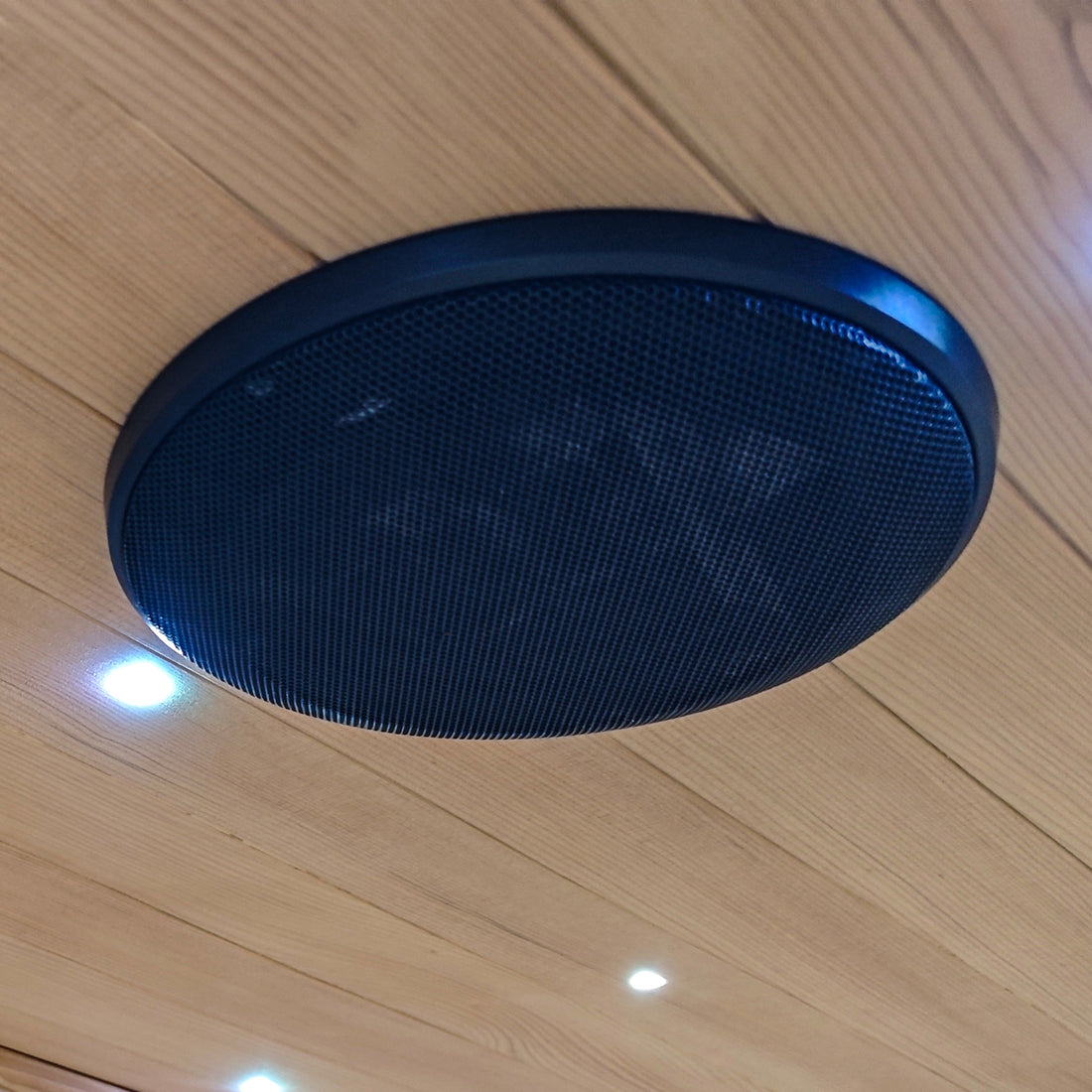 Round black ceiling speaker installed in a wood-paneled ceiling