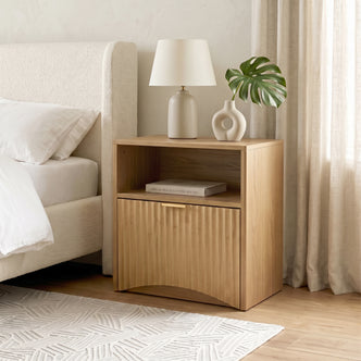 Light oak nightstand styled beside a bed in a modern bedroom.