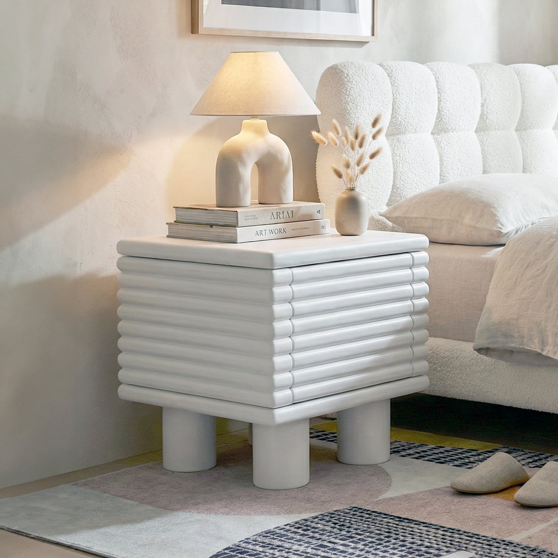 White ribbed nightstand in bright bedroom setting with lamp, vase and books