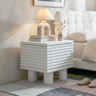 White ribbed nightstand in bright bedroom setting with lamp, vase and books