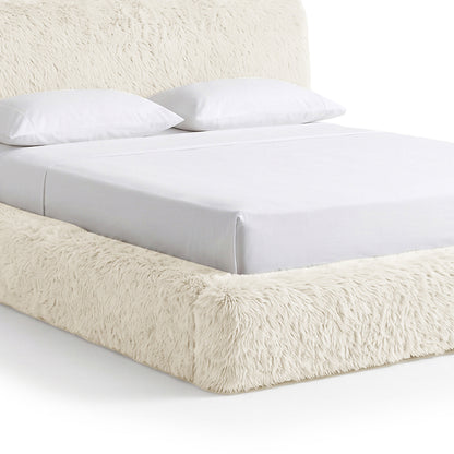 Partial view of a plush upholstered bed on a white background.