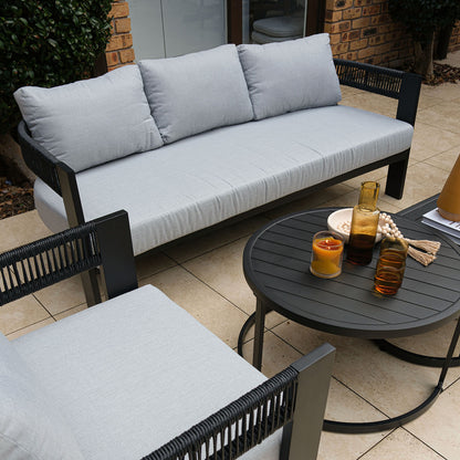 Outdoor patio furniture with gray cushions on black frame, coffee table with drinks and decor on a tiled patio
