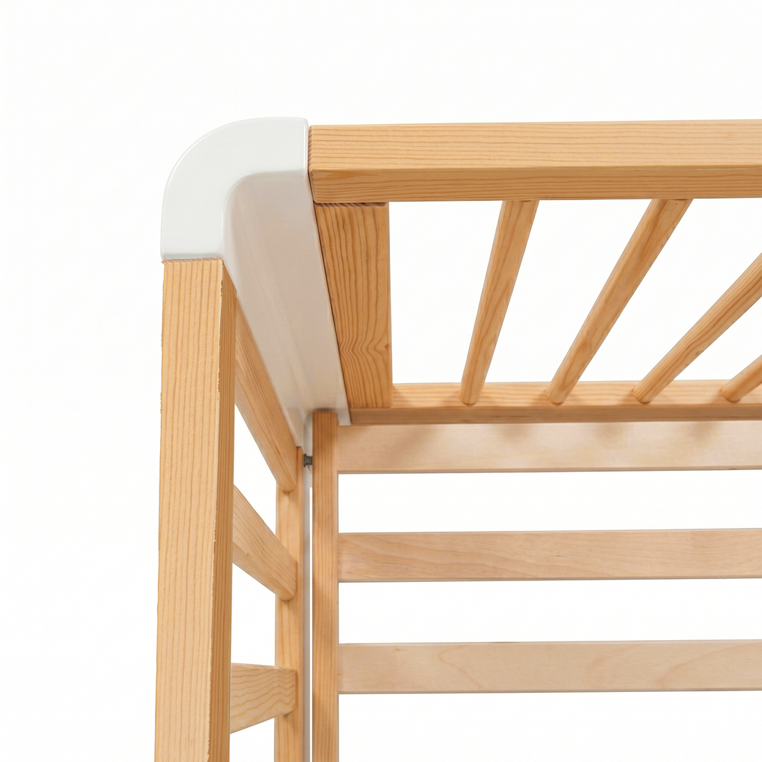 Close-up of top corner and slats of wooden crib with white accent on white background