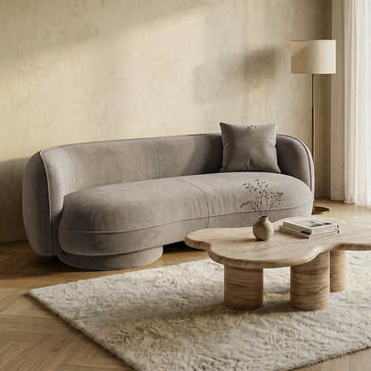 Light gray curved sofa styled in living room with coffee table and rug