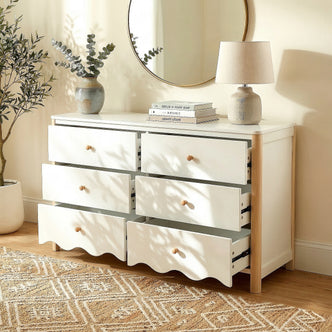 White and wood six-drawer dresser in a bright room with vase, lamp, mirror, plant, and open drawers