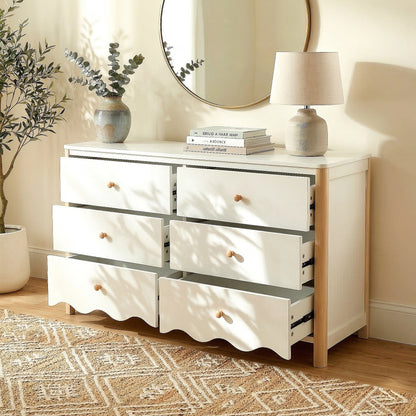 White and wood six-drawer dresser in a bright room with vase, lamp, mirror, plant, and open drawers