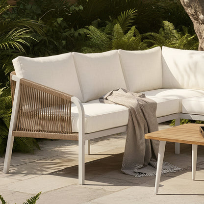 Outdoor lounge with Vernon Sofa Cushion Covers in Cream White on a curved sectional. Features woven rope frame and textured gray throw. Lush foliage backdrop enhances the tranquil setting.
