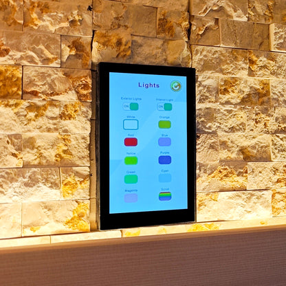 Black-framed touchscreen control panel mounted on a patterned stone wall.