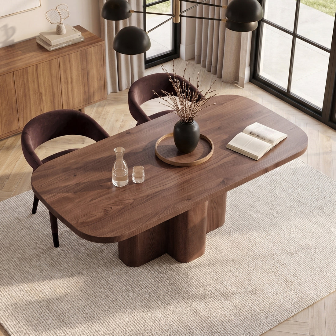 Wooden dining table styled in a warm modern room with rug, chairs, and decor.