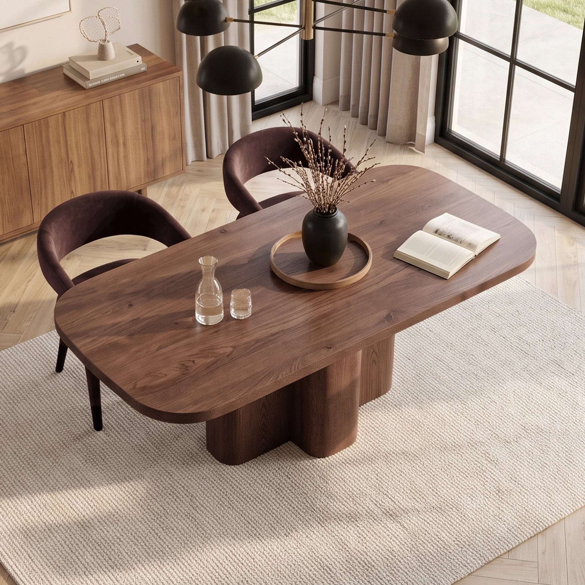 Wooden dining table styled in a warm modern room with rug, chairs, and decor.