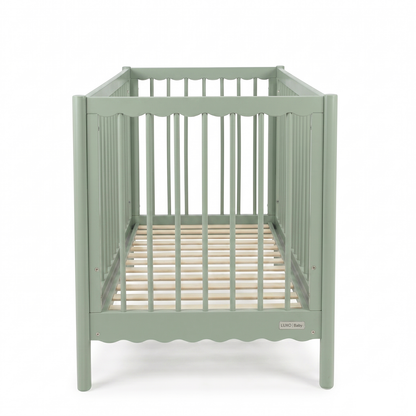 Sage green baby crib viewed from short end on white background