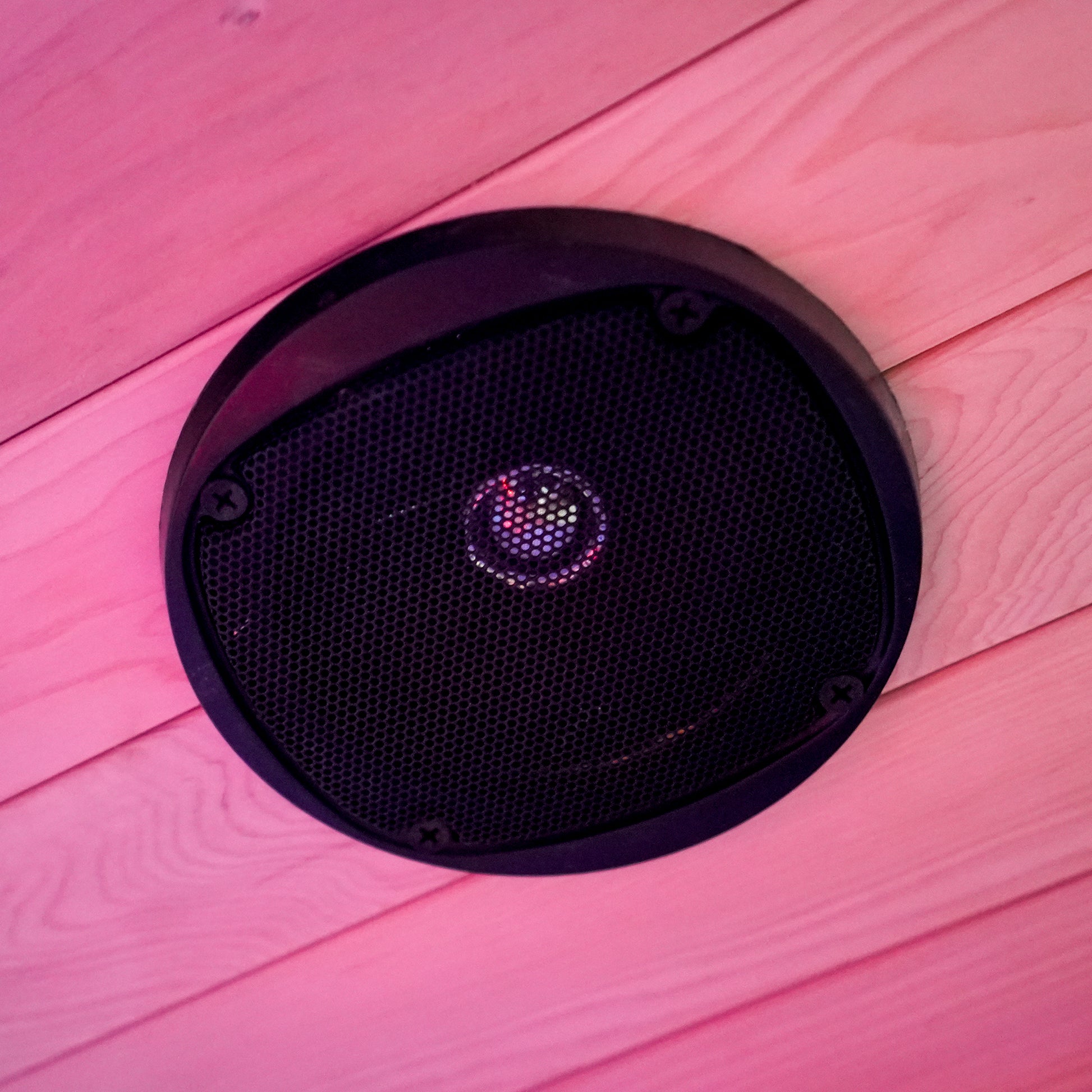Round black speaker mounted in a wood-paneled interior with ambient lighting