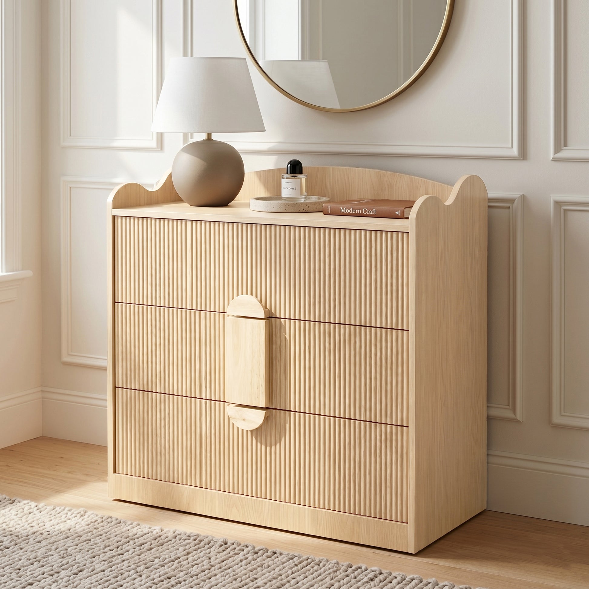 Three-drawer wooden dresser in a bedroom setting with lamp, mirror, and decor