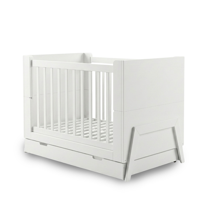 White baby crib on white background showing full product with solid panels, vertical slats, pull-out drawer and angled legs