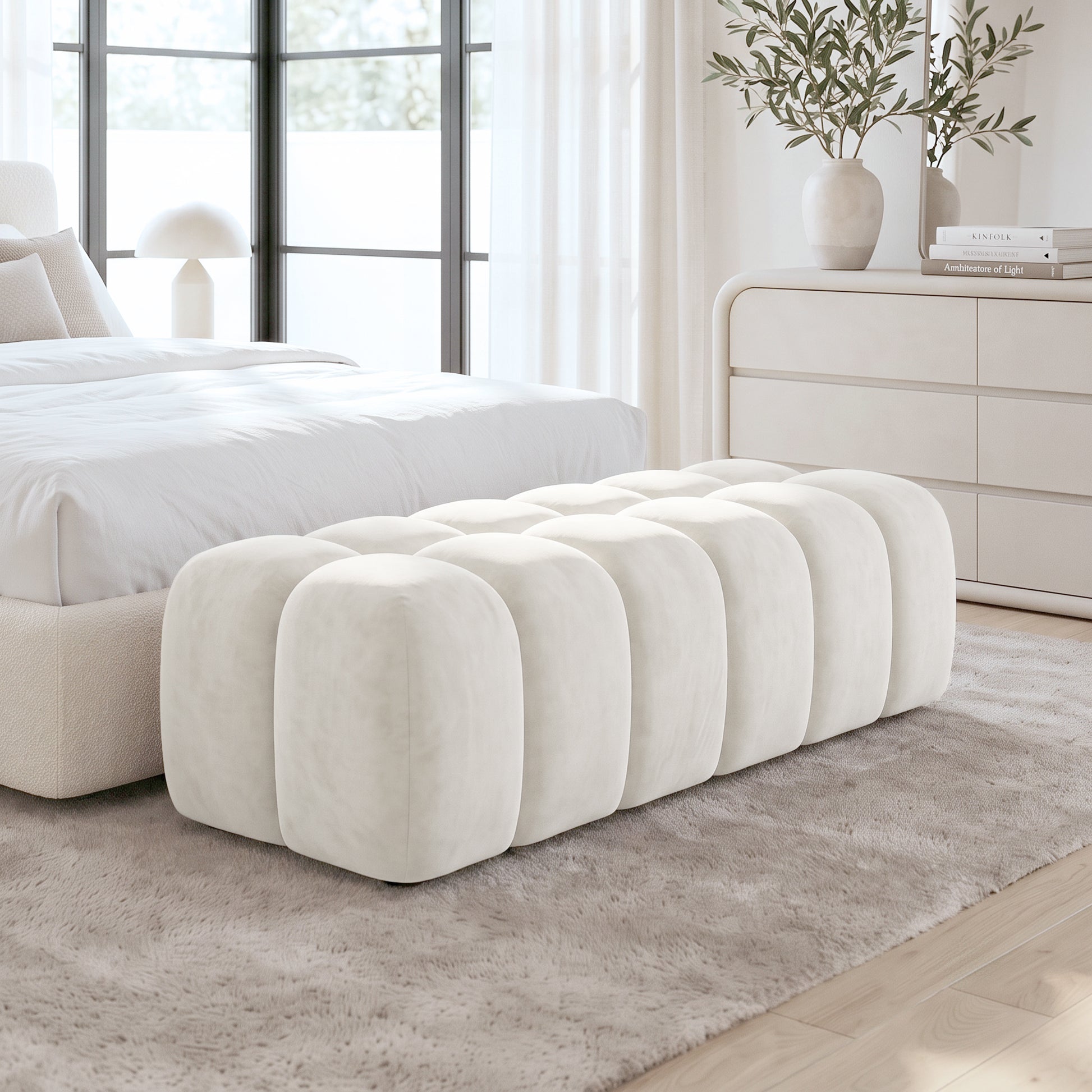 Light beige upholstered ottoman bench at the foot of a bed in a bright bedroom