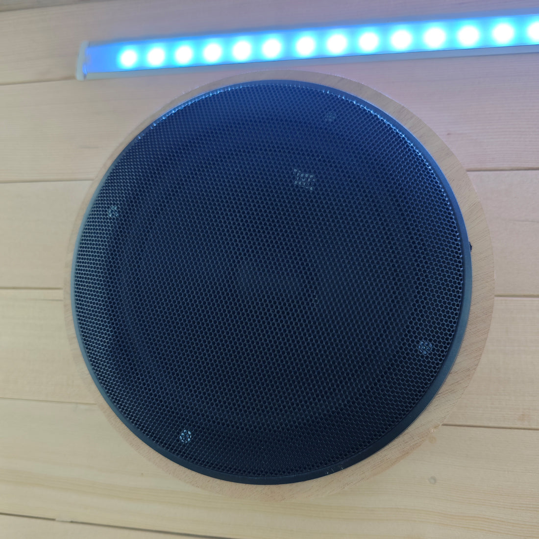 Black circular speaker installed in a wood-paneled surface with blue LED light above