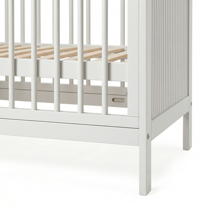 Close-up of the corner section of a white baby crib showing slatted side and wooden base