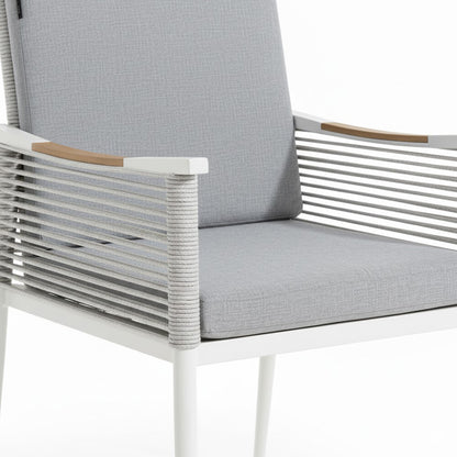 Casara 7 Piece Outdoor Dining Set in White & Grey features a modern armchair with a white metal frame, light-gray rope cord back, and wooden armrest accents, complemented by matching cushions.