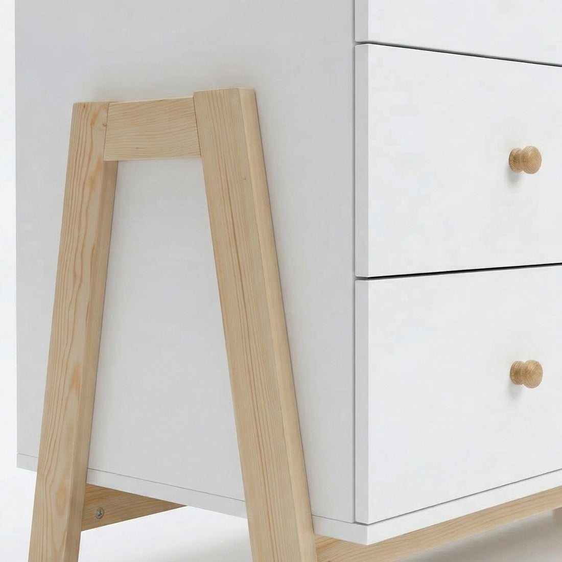 Close-up view of white dresser’s lower section with wooden legs and knobs on white background