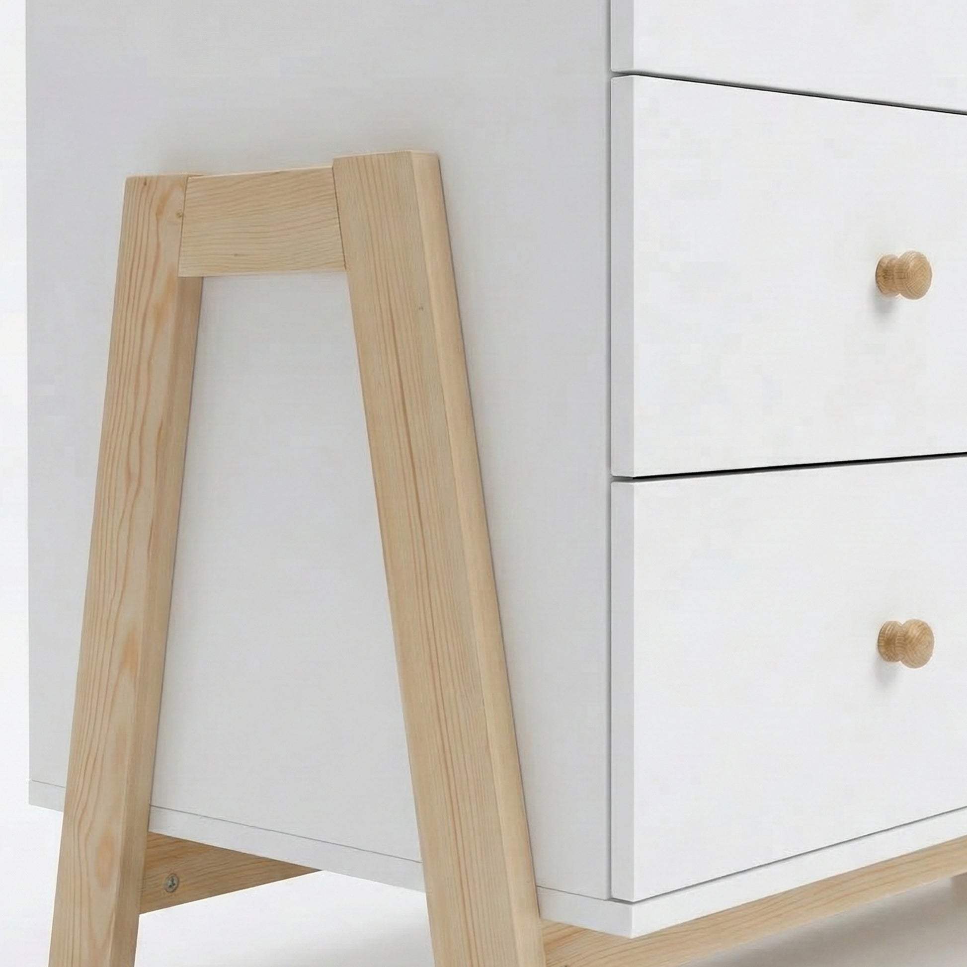 Close-up view of white dresser’s lower section with wooden legs and knobs on white background