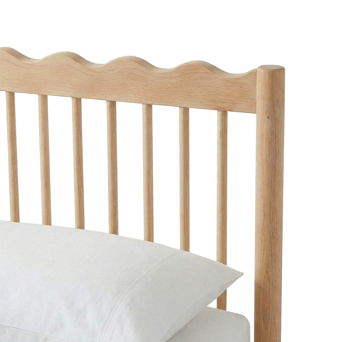 Close-up of bed frame headboard with scalloped edge and two pillows on white background