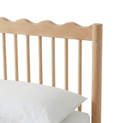Close-up of bed frame headboard with scalloped edge and two pillows on white background