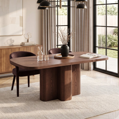 Modern wooden dining table styled in a bright room with chairs, decor, and large windows.