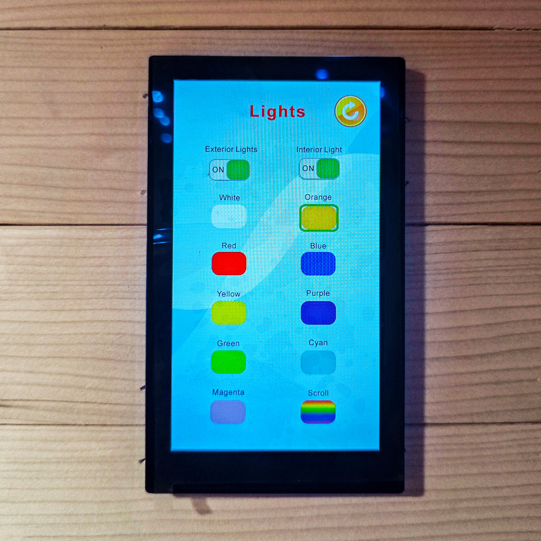 Touchscreen lighting control panel mounted on a wooden background.