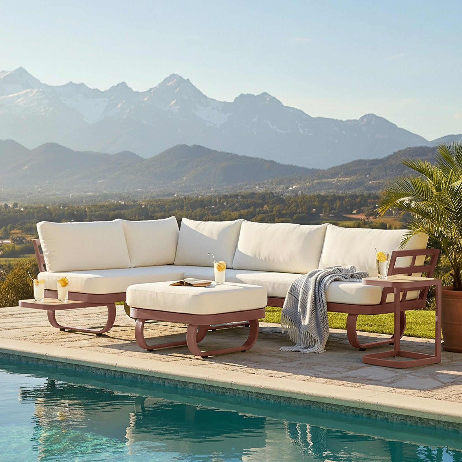 Paloma Modular Outdoor Lounge Set in Terracotta featuring a light-cream cushioned L-shaped sectional with a matching ottoman, reddish-brown metal frames, small side table with lemonade, and a draped gray throw.